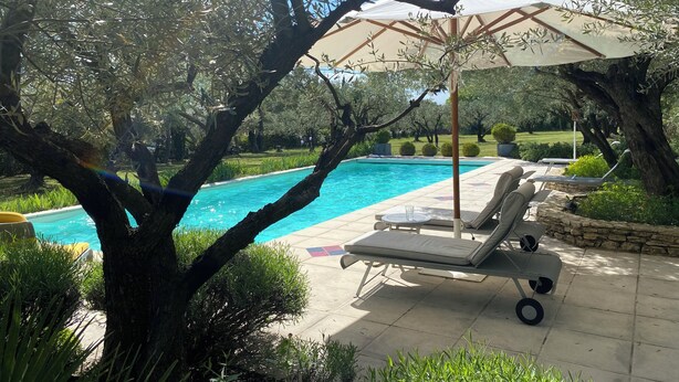 Et poolområde med liggestole, en parasol og en klar, blå pool.
