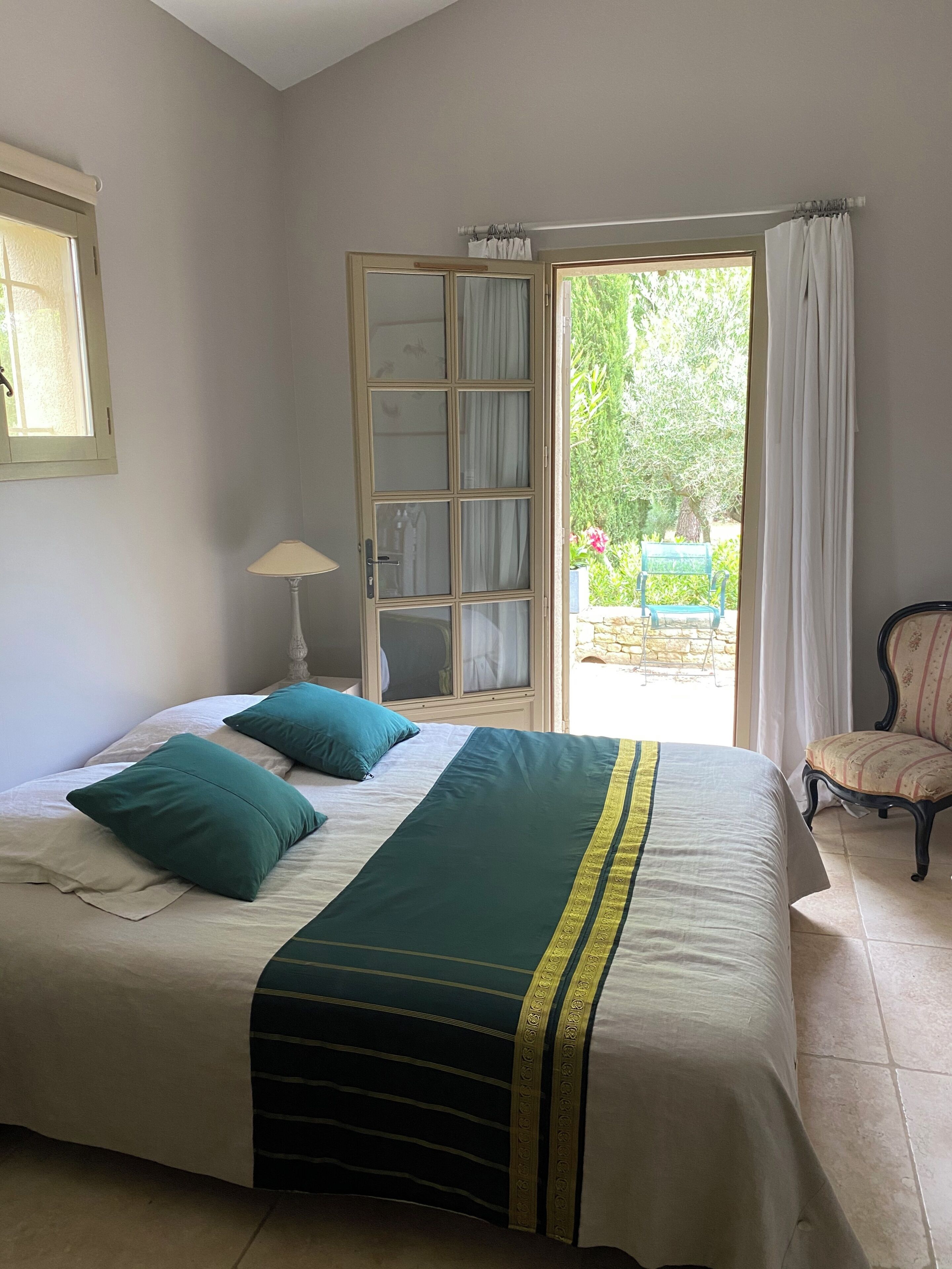 Un dormitorio con una cama, una silla, una lámpara y vistas al exterior.