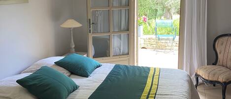 Un dormitorio con una cama, una silla, una lámpara y vistas al exterior.