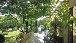 En overdækket terrasse med stenvægge, udendørs møbler og udsigt til en græsplæne og pool.