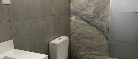 Moderni kylpyhuone, jossa on valkoinen wc-istuin, marmoriseinä ja valkoinen pesuallas.