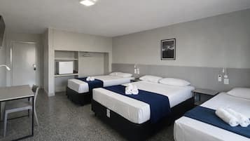 A hotel room with three beds, a desk, a chair, a small refrigerator, and a picture on the wall.