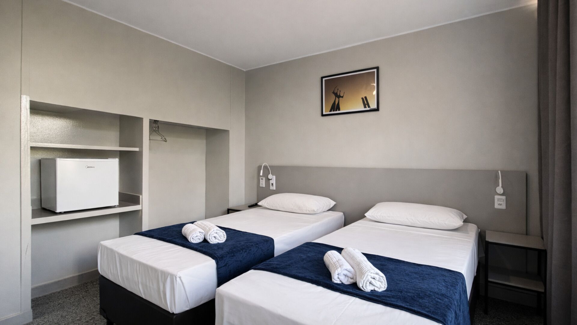 A hotel room with two beds, a minibar, and a painting on the wall.