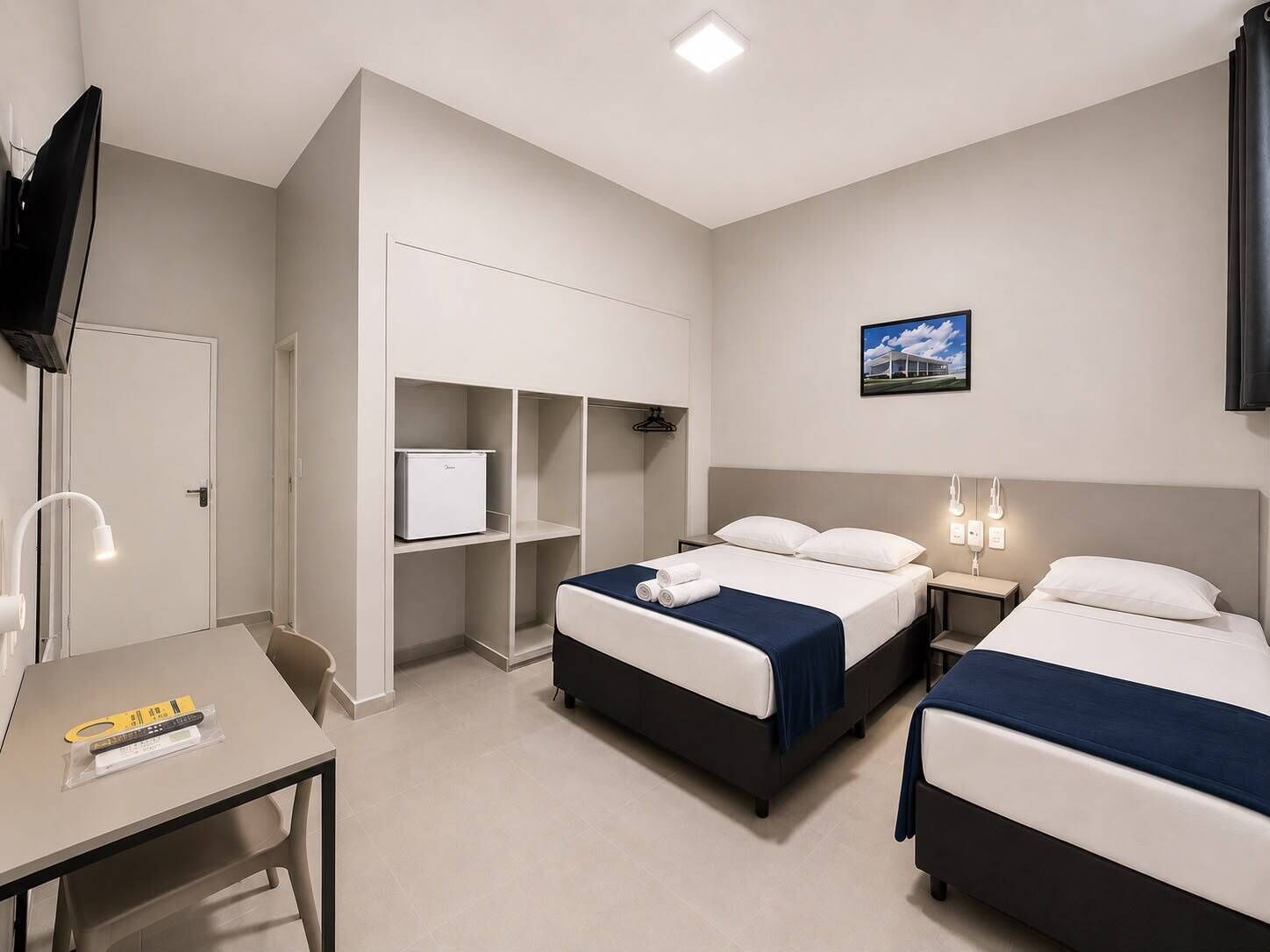 A hotel room with two beds, a desk, a TV, and a small refrigerator.