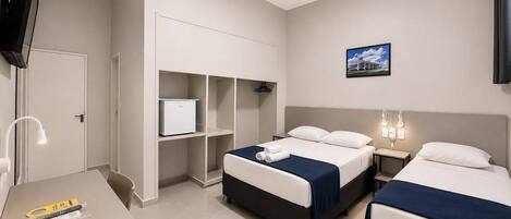 A hotel room with two beds, a desk, a TV, and a small refrigerator.