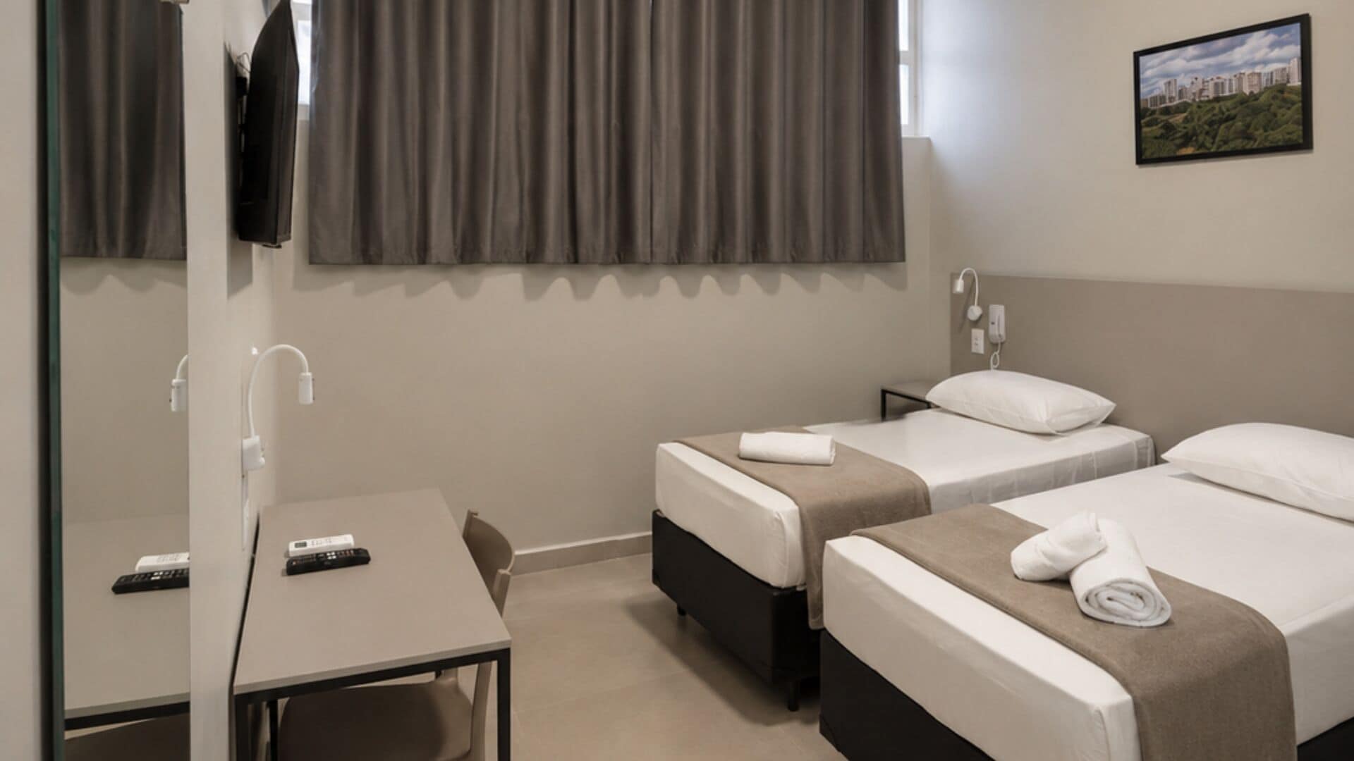 Habitación de hotel con dos camas, un escritorio, una silla, un televisor y una ventana con cortinas.