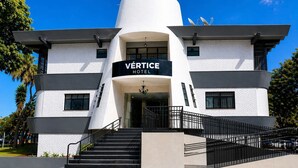Un hotel moderno con un letrero llamativo que dice 'VERTICE HOTEL', que presenta una estructura cilíndrica distintiva, múltiples ventanas y una escalera que conduce a la entrada.