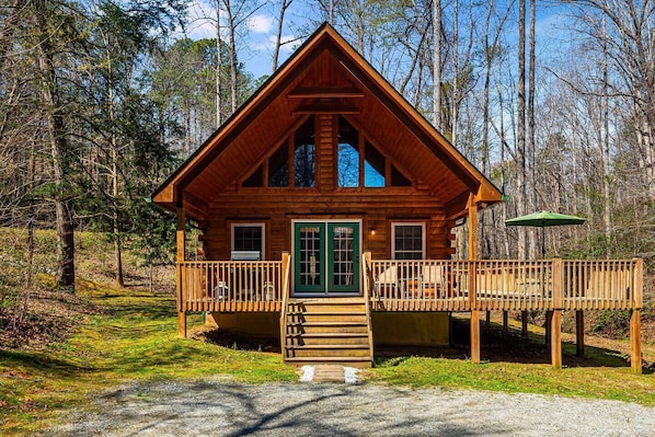 Une cabane en bois avec un porche à l’avant, une porte verte et une terrasse.