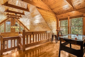 A wooden interior with a pool table, wooden flooring, and large windows.