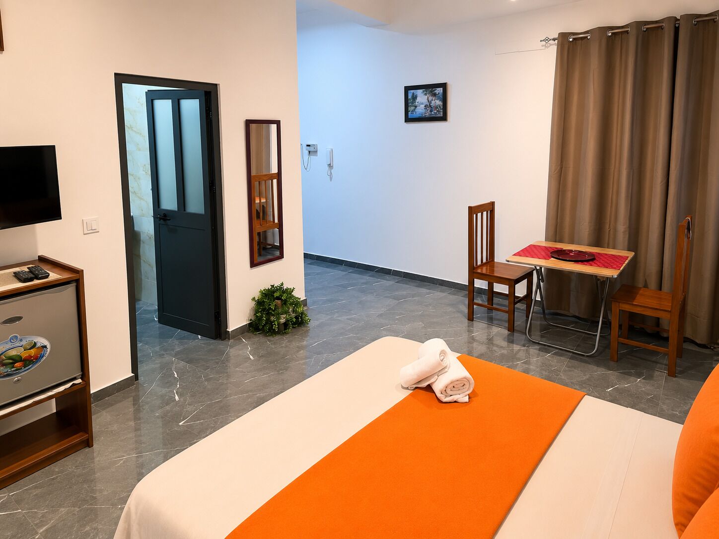 A hotel room with a bed, a desk, a chair, a TV, and a small kitchenette.