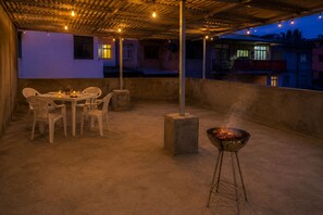 An outdoor patio with a grill, chairs, and a table set for dining. - Praia City Apartments (Praia)