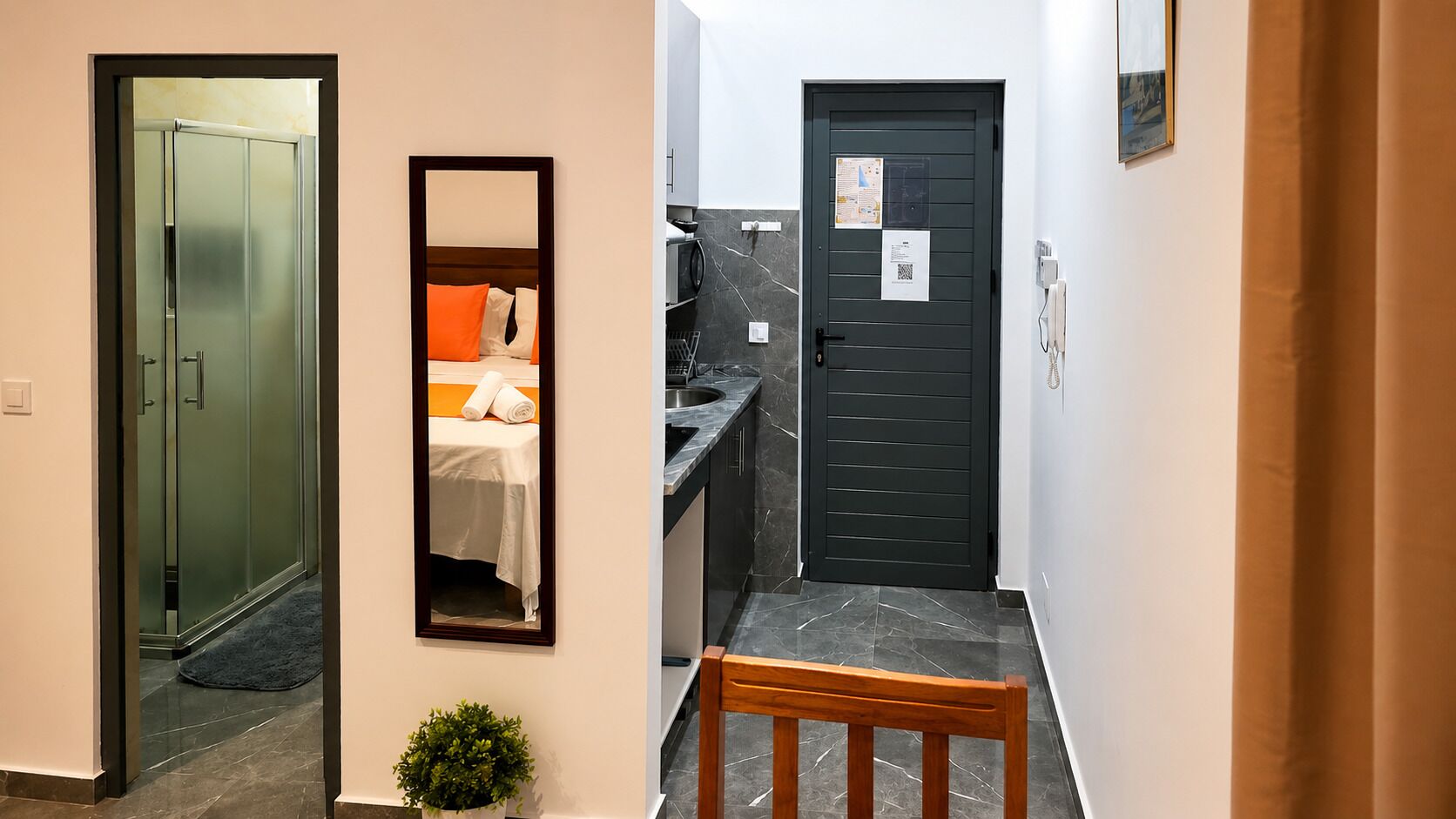 Un couloir d’hôtel avec un lit, un miroir, une porte et un banc.