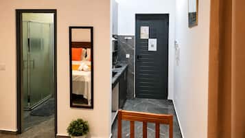 Un couloir d’hôtel avec un lit, un miroir, une porte et un banc.