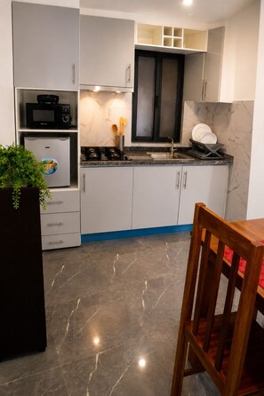 A modern kitchen with white cabinets, a black microwave, a gas stove, and a sink. - Praia City Apartments (Praia)