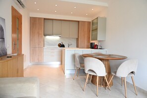 A modern kitchen with a central island, white cabinetry, and a dining area with a round table and chairs. - Sunny 2 bedroom close to beach (Albufeira)