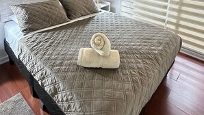 Una cama bien hecha con un edredón acolchado, una toalla enrollada y una lámpara de noche.
