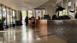Un vestíbulo amplio con una mesa de recepción, ventanas grandes y plantas en macetas.