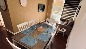 Un comedor con una mesa de madera, sillas blancas y un mantel tejido.