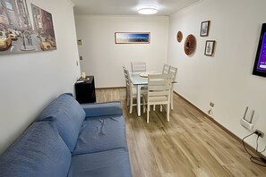 A living room with a blue sofa, a dining table with chairs, a small black cabinet, and a framed picture on the wall. - Spacious apt. 3 bedrooms. Fully equipped downtown Stgo (Santiago)