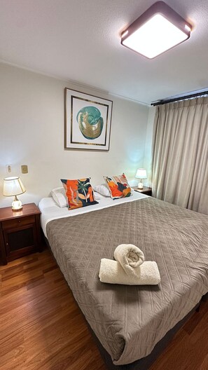A hotel room with a bed, two bedside tables with lamps, a framed artwork above the bed, and a window with curtains. - Spacious apt. 2 bedr. Fully equipped downtown Stgo. (Santiago)