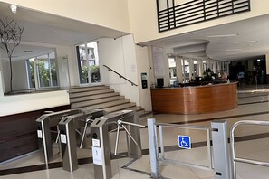 Um lobby moderno com uma mesa de recepção, uma escadaria e um sinal de acessibilidade para pessoas com deficiência.