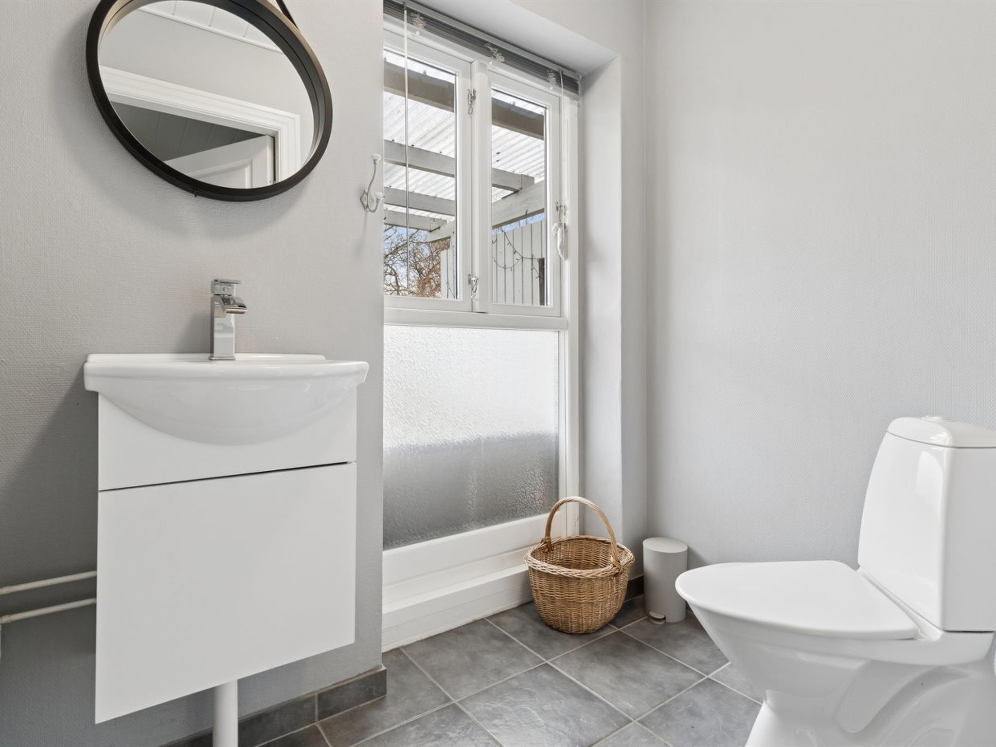 A bathroom with a white sink, a toilet, a mirror, and a window with a view of the outside.