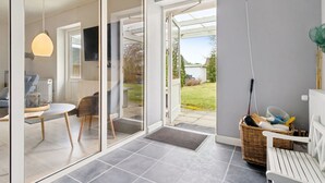 En modern inredning med en glasdörr som leder ut till en uteplats, en matplats med bord och stolar samt en korg av rotting som innehåller diverse föremål.