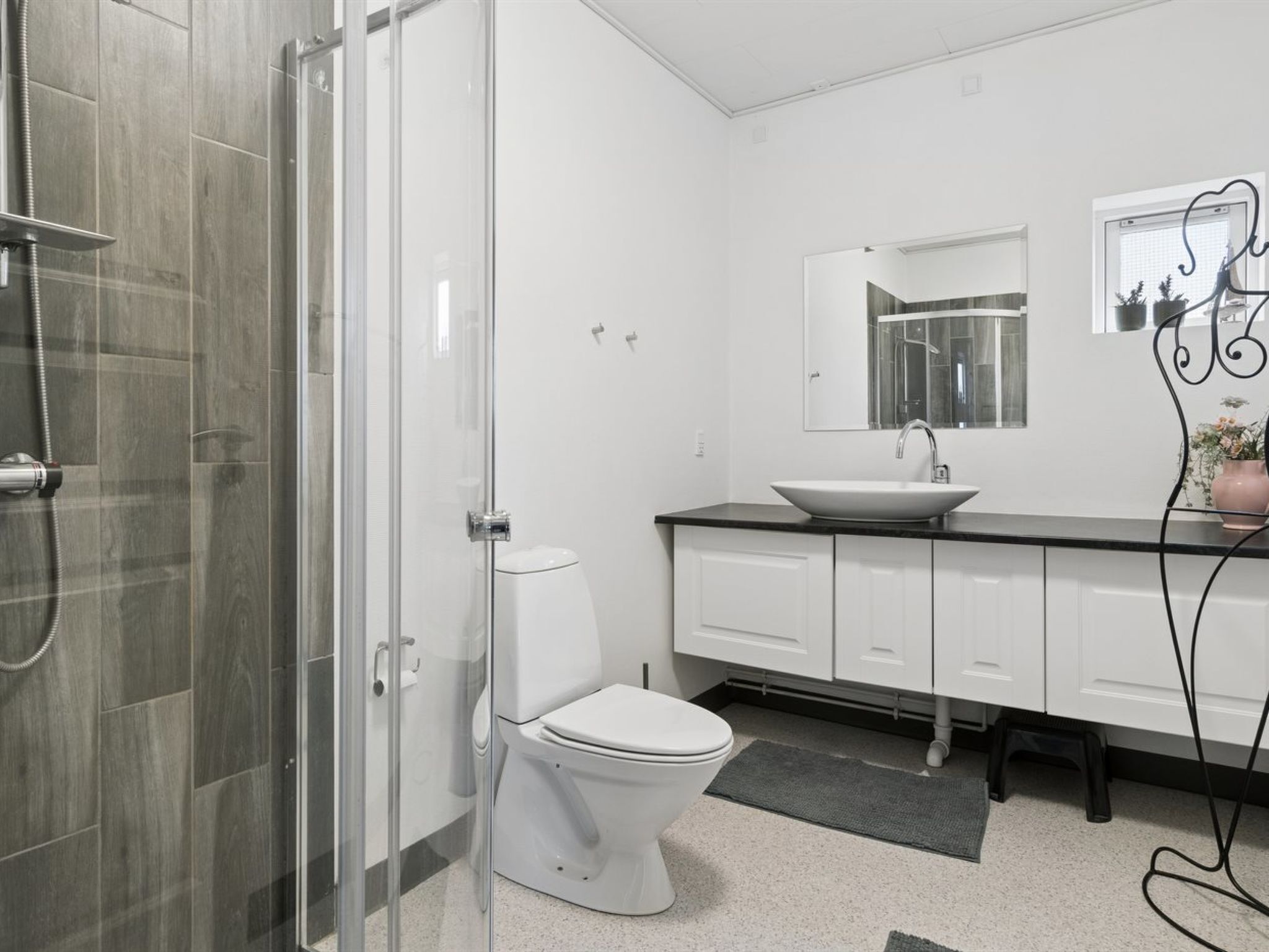 Une salle de bain moderne avec une douche à l’italienne en verre, des toilettes blanches, un lavabo sur colonne et un grand miroir au-dessus du lavabo.