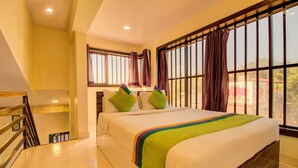 A hotel room with a bed, a window with curtains, a staircase, and a view of the outside.