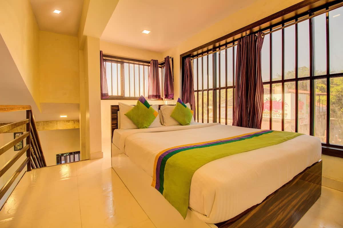 A hotel room with a bed, a window with curtains, a staircase, and a view of the outside.