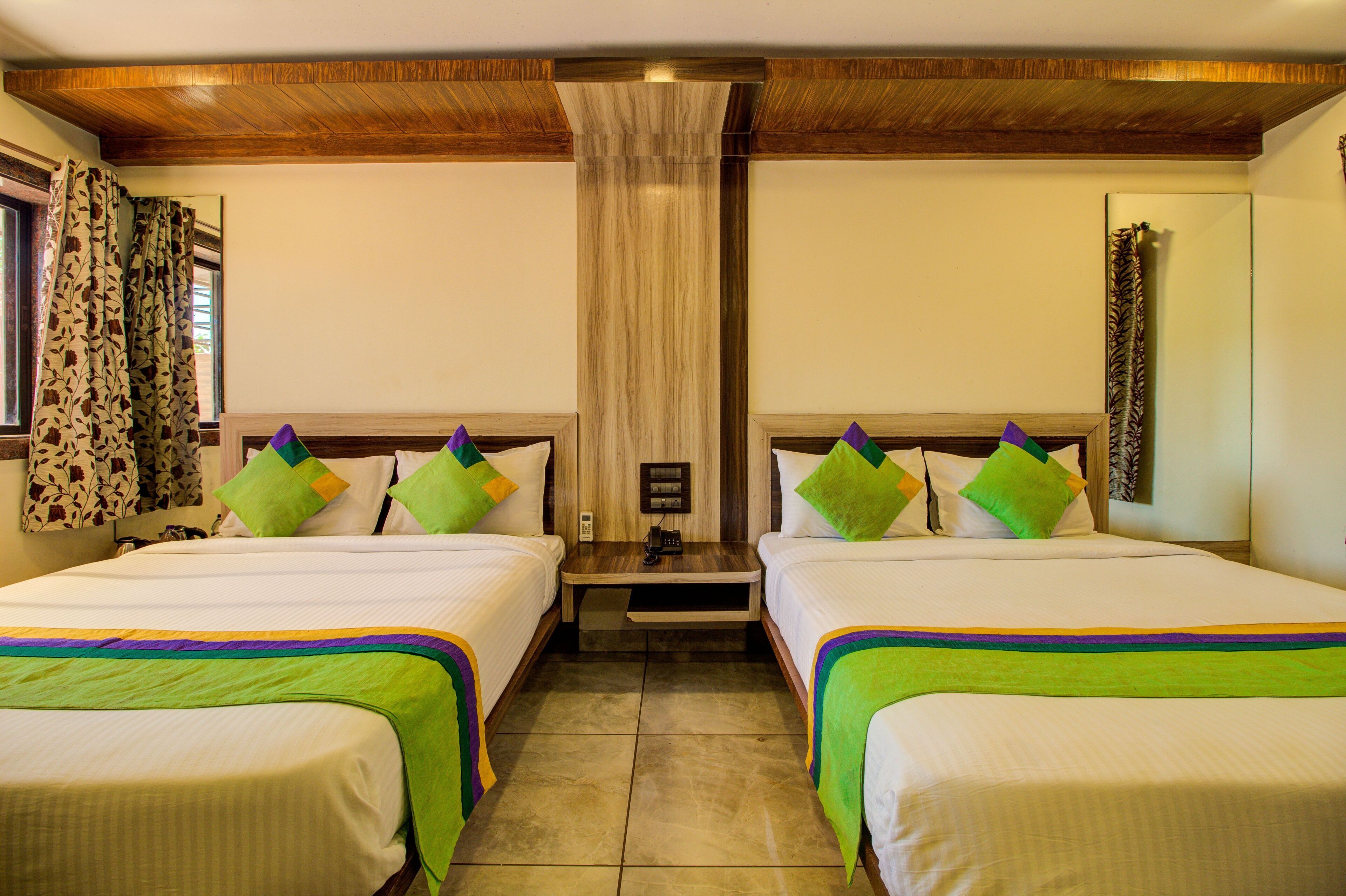 A hotel room with two beds, a wooden ceiling, a nightstand, and a curtain.