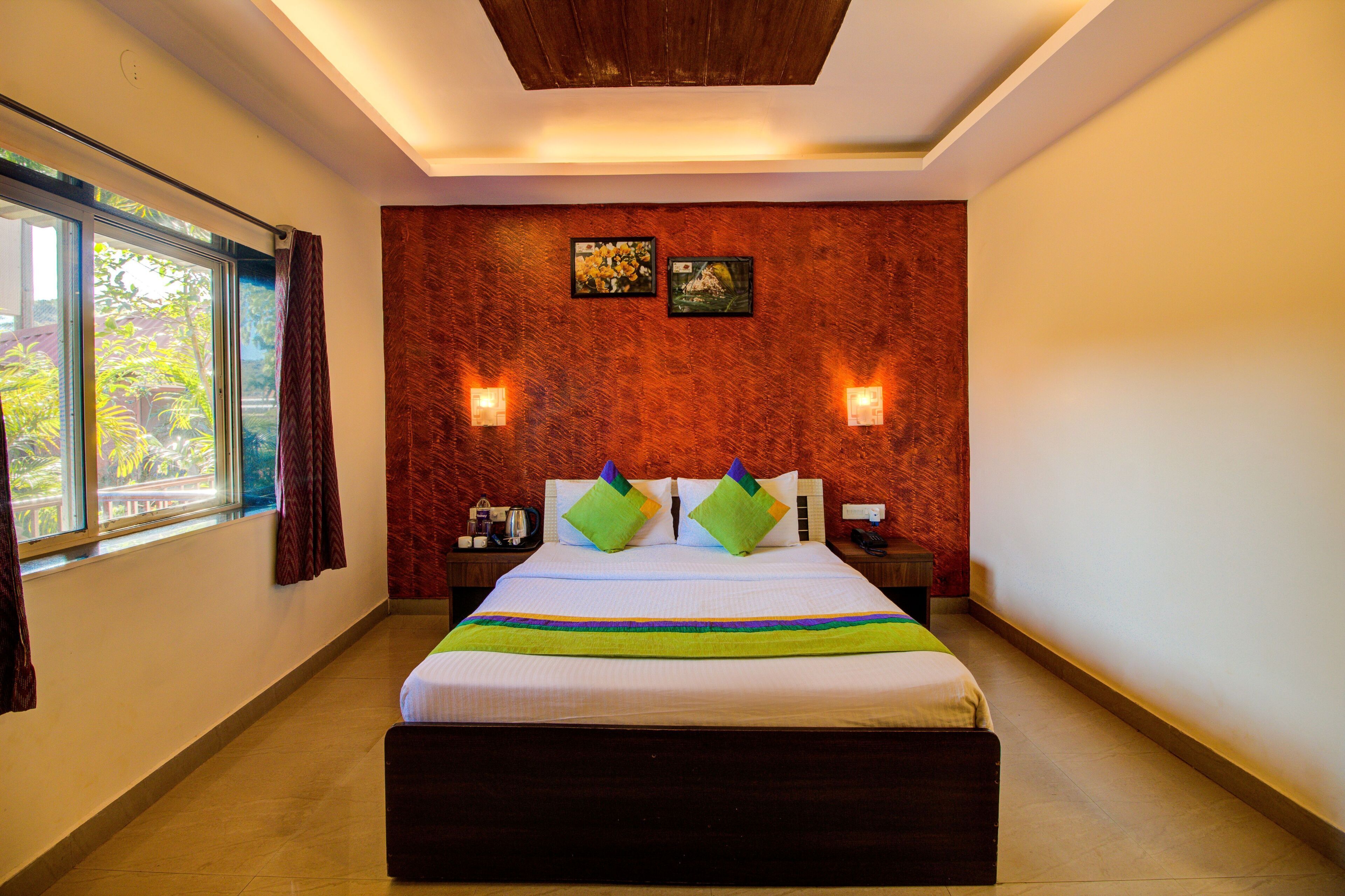 Habitación de hotel con una cama grande, dos luces fijadas a la pared, un ventanal con cortinas y techo de madera.