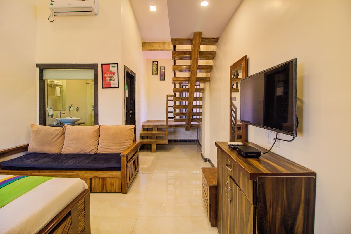 A compact room with a bed, a TV, a wooden staircase, and a bathroom.