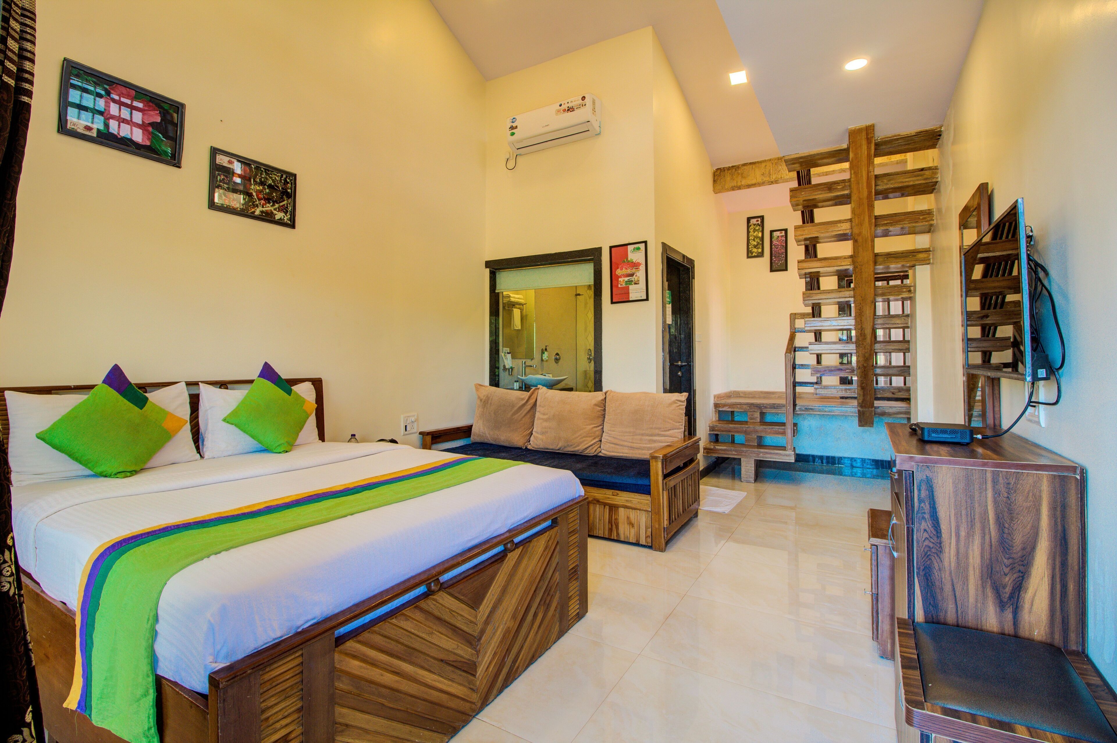 A bedroom with a bed, a sofa, a TV, and a wooden ladder.
