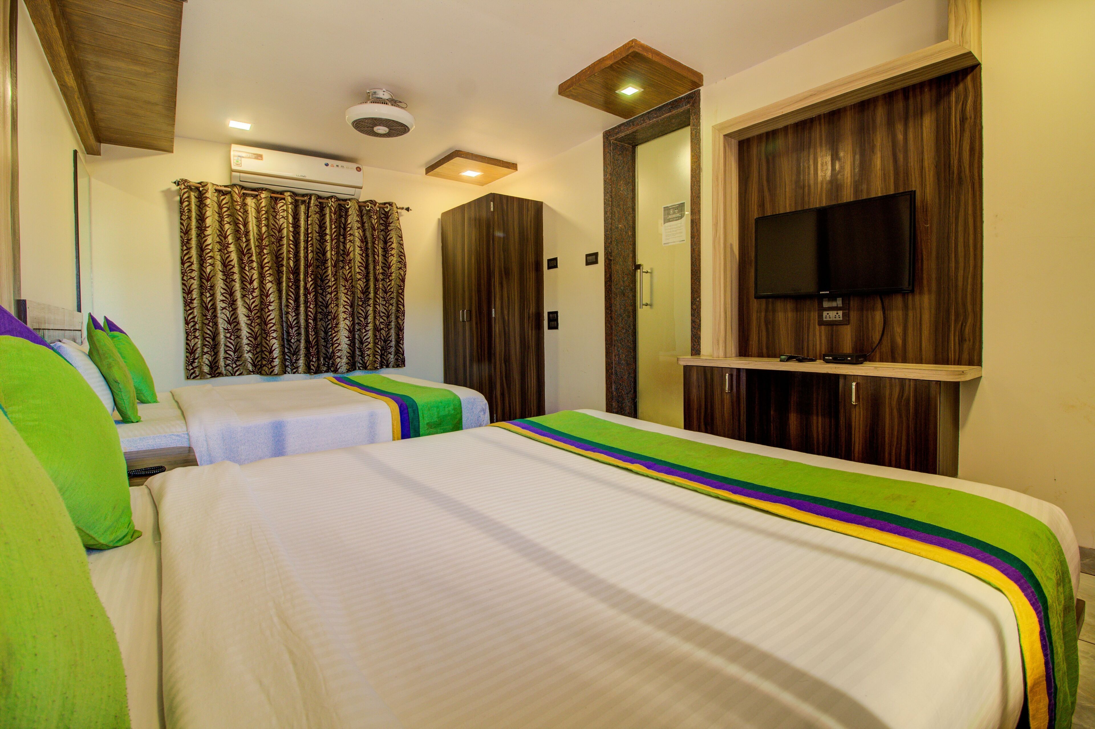 Une chambre d’hôtel avec deux lits, une télévision, un appareil de climatisation et une armoire en bois.
