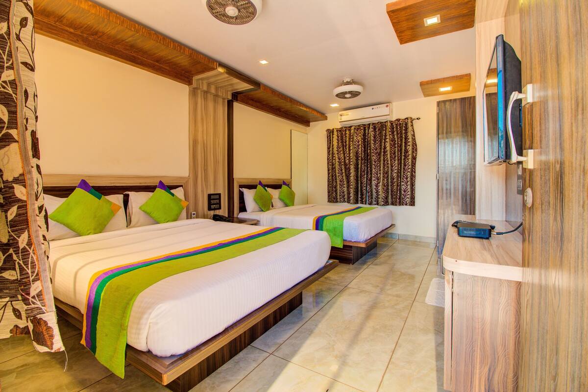 A hotel room with two beds, a TV, an air conditioning unit, and a wooden desk.