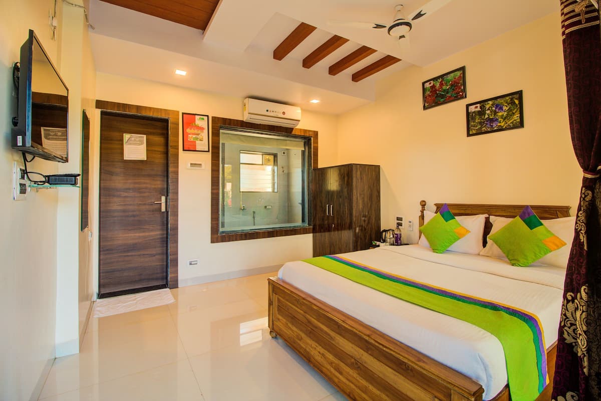 A hotel room with a bed, a wardrobe, a mirror, an air conditioning unit, and a window.