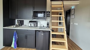 A modern kitchen with dark cabinets, a microwave, a toaster, and a dishwasher. There is a wooden ladder leading to a lofted area. - Northern Lights Cabin - Syðribrú (Selfoss)