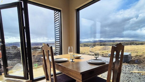 A dining area with a wooden table and chairs, large windows, and a view of a landscape. - Northern Lights Cabin - Syðribrú (Selfoss)