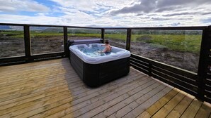 A hot tub on a wooden deck with a view of a grassy field and mountains. - Northern Lights Cabin - Syðribrú (Selfoss)