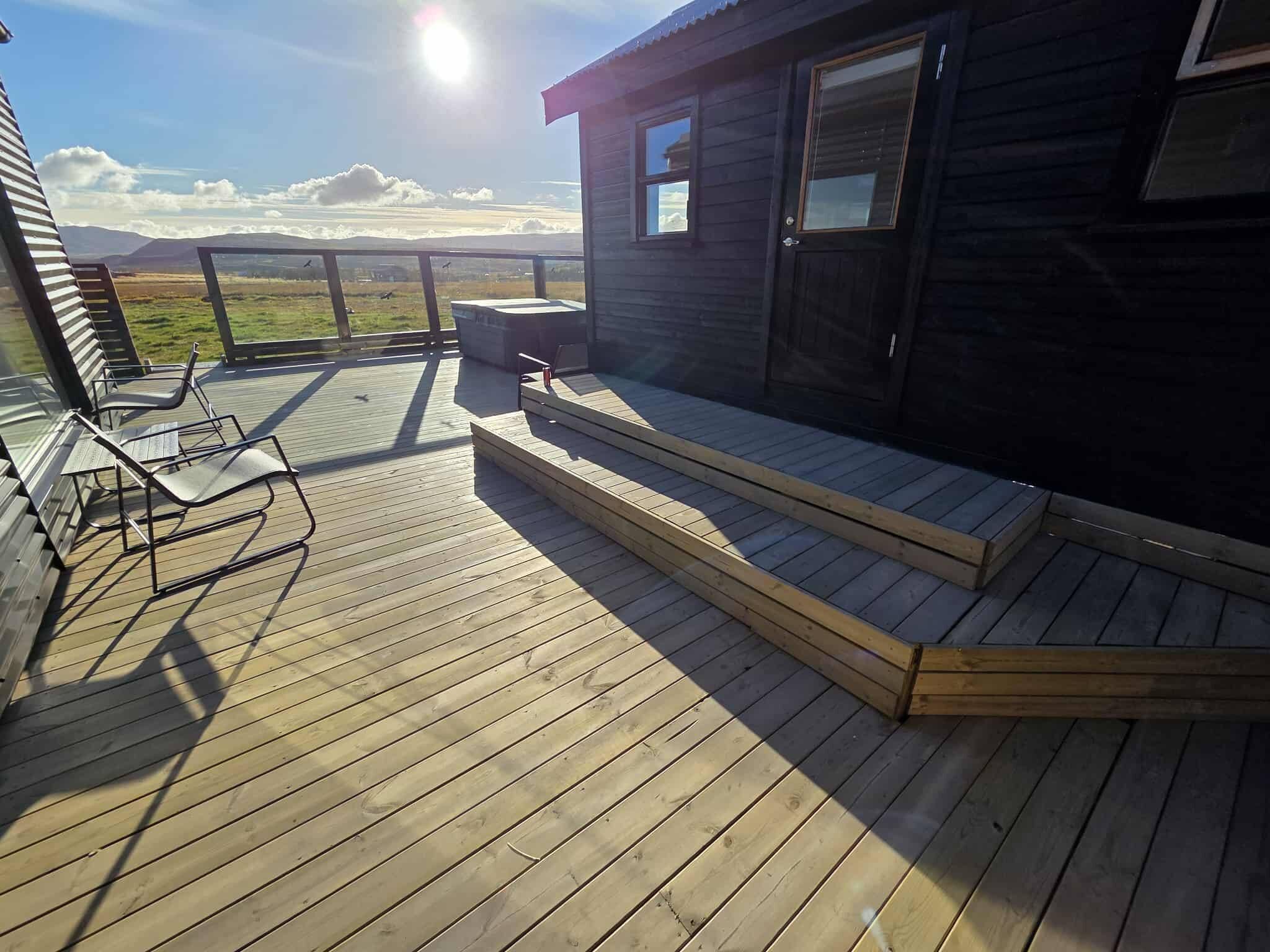 A wooden deck with steps leading to a cabin, a chair, and a view of the landscape.
