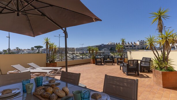 Una terraza en la azotea con sillones de descanso, una mesa con comida y plantas en macetas.