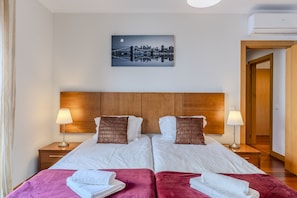 Ein Hotelzimmer mit zwei Betten, einem Stadtbildgemälde, einem Holzkopfstütze und einer Klimaanlage.