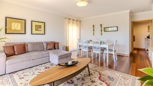 Una sala de estar con sofá, mesa de centro, mesa de comedor, sillas y un tapete estampado.