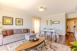 Ein Wohnzimmer mit einer Couch, Couchtisch, Esstisch, Stühlen und einem gemusterten Teppich.