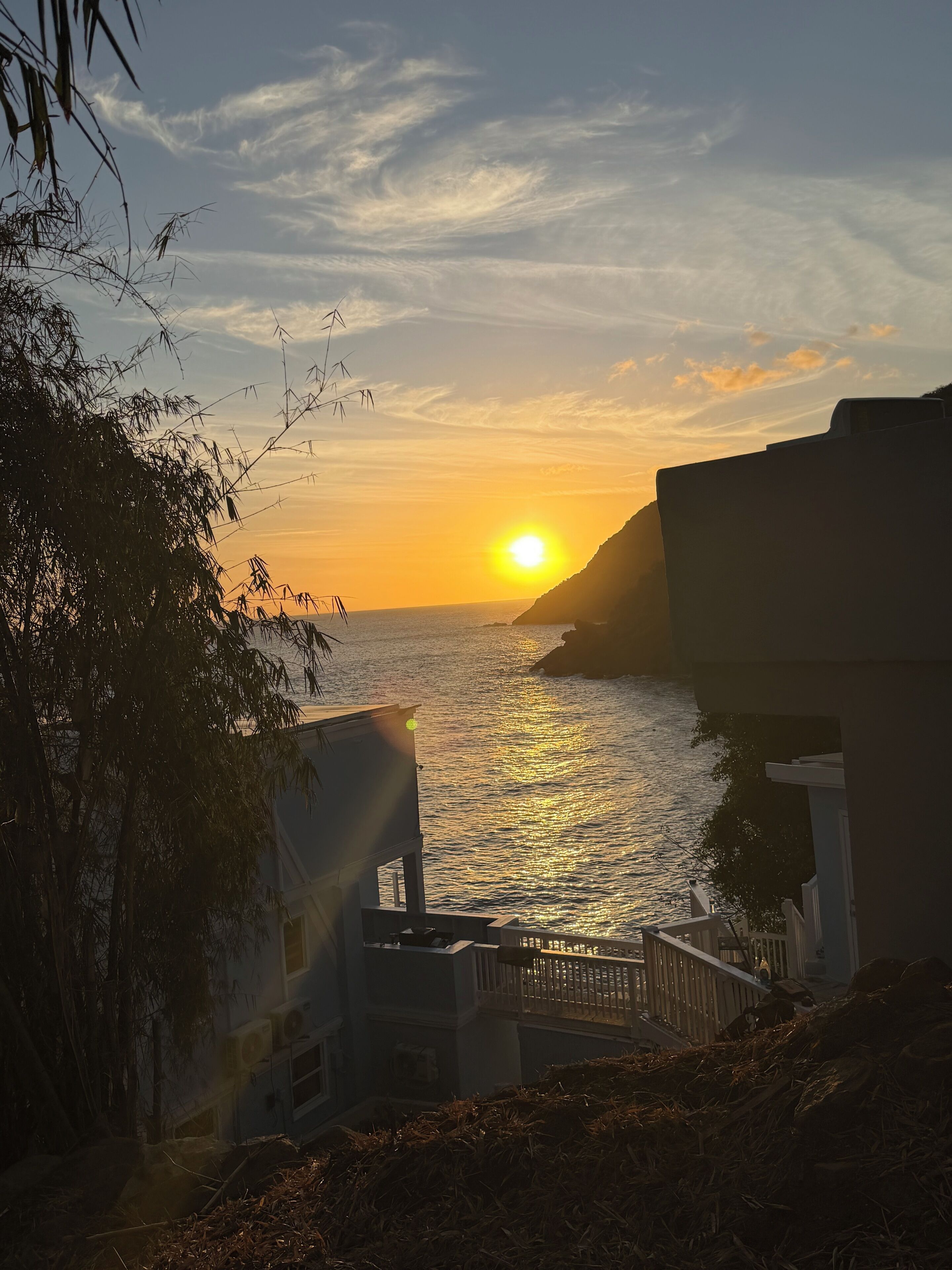 Une vue sur le coucher de soleil en bord de mer, avec un bâtiment et un escalier menant à un balcon.