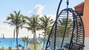 Uma cadeira suspensa com almofadas, um sofá com um travesseiro rosa e vista para a praia e oceano.