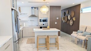 Eine moderne Küche mit einer zentralen Kochinsel, Holzstühlen, einem Kronleuchter und einer Sitzecke mit Sofa und Sesseln.