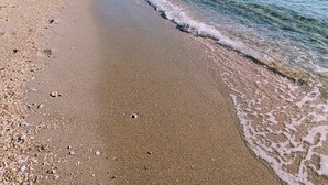 Ein Strand mit klarem Wasser, Kieselsteinen und einem Gebäude in der Ferne.
