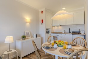 A modern kitchen with white cabinets, a dining table set with plates, cups, and a fruit bowl. - #319 Cozy 1 Bedroom Apartment | Pool & Relaxation (Albufeira)